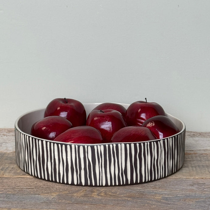 White bowl with black zebra pattern containing red apples on a wooden surface.