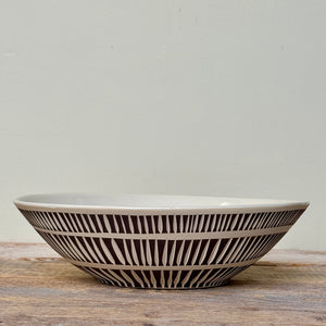 Ceramic bowl with black striped pattern on a wooden surface