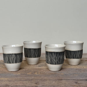Four ceramic cups with black patterned bands on a wooden surface