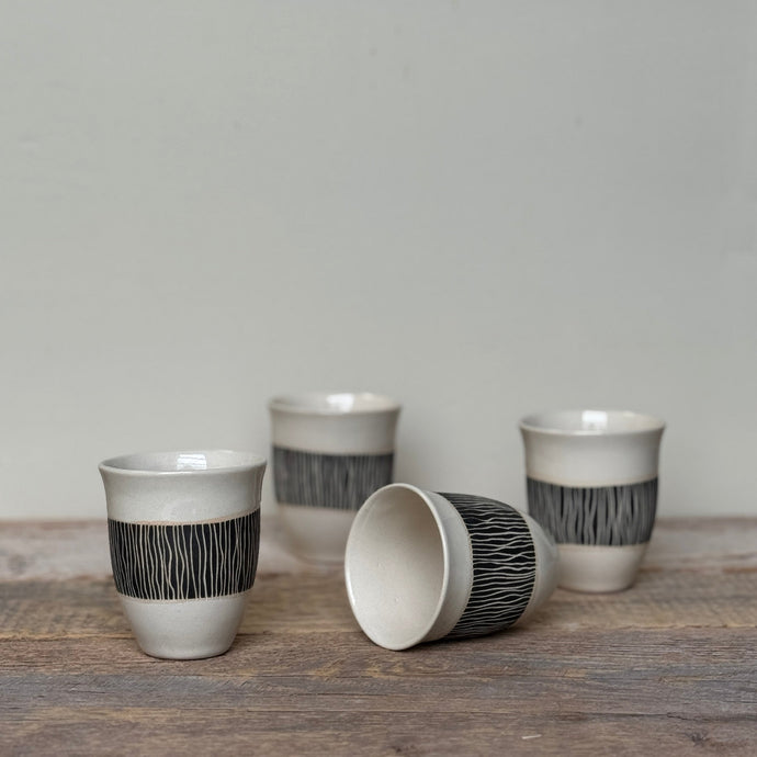 Set of ceramic cups with black and white patterns on a wooden surface.