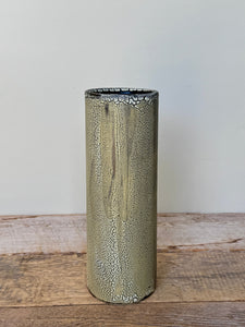 Cylindrical metallic vase with textured surface on a wooden surface